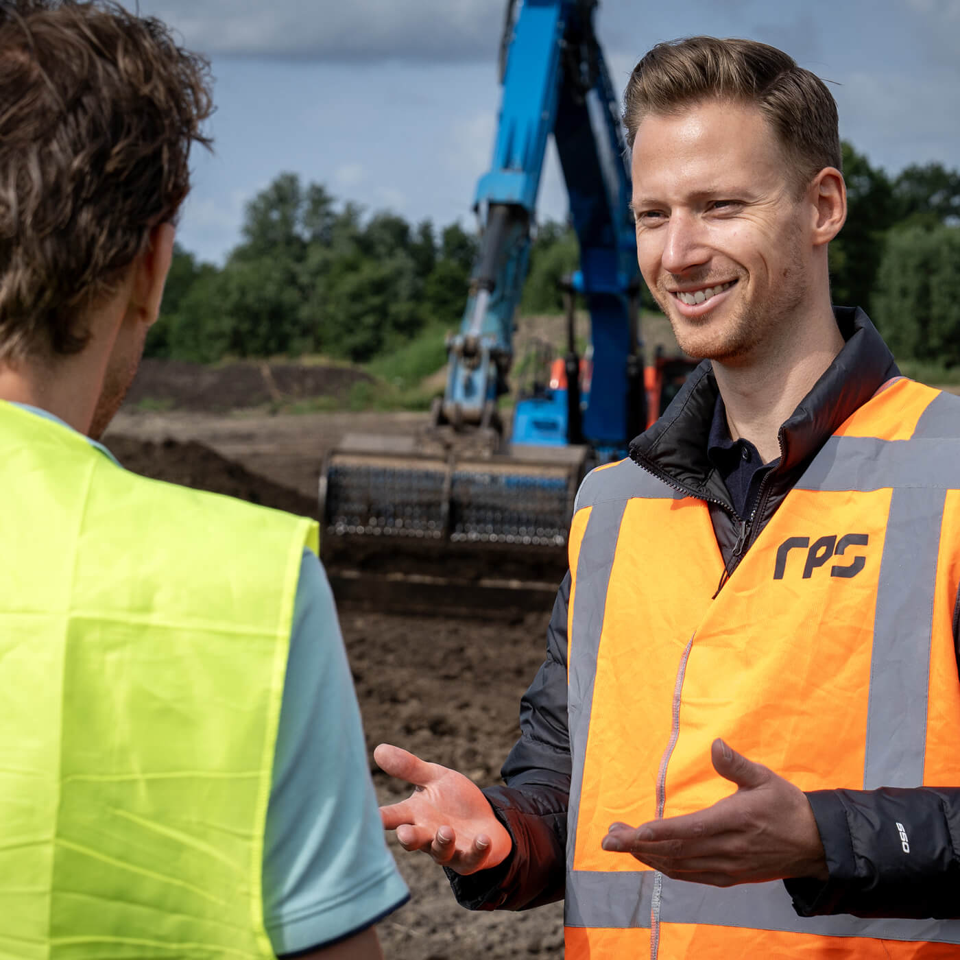 RPS-medewerker in gesprek met een klant op een projectlocatie, met een graafmachine op de achtergrond. bekijk onze vacatures